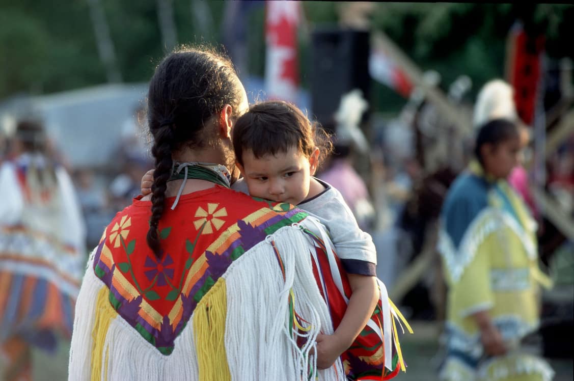 Indigenous person with baby surrounded by other blurred Indigenous people in the background