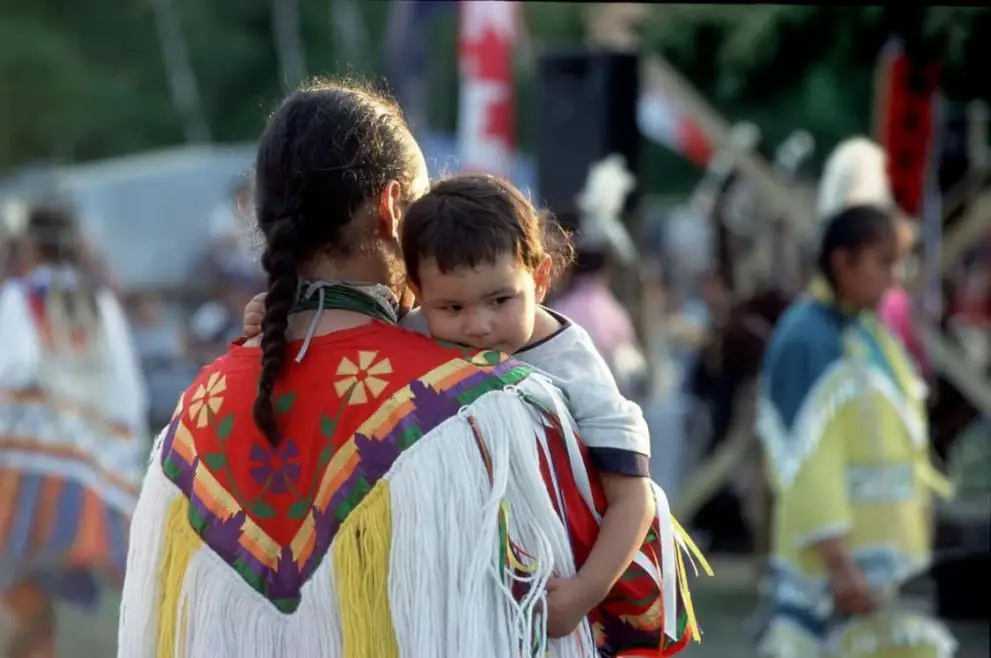 Femme des Premières Nations en costume traditionnel portant son enfant malade
